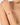 Close-up of a woman's arm wearing a gold bracelet with red beads on a neutral background