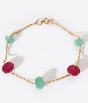 Bracelet with gold chain and green and red beads on a white background