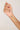 Hand holding a delicate gold necklace with small colored beads against a plain background