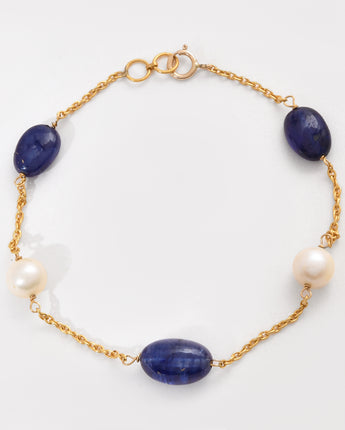 Gold bracelet with blue stones and pearls on a white background