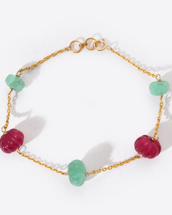 Bracelet with gold chain and green and red beads on a white background