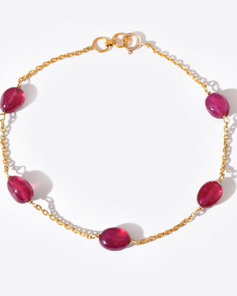 Gold bracelet with red gemstones on a white background