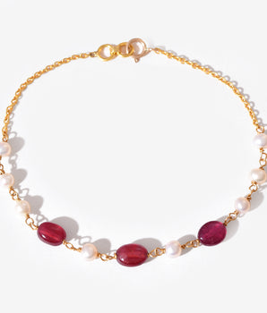 Gold bracelet with red gemstones and white pearls on a white background