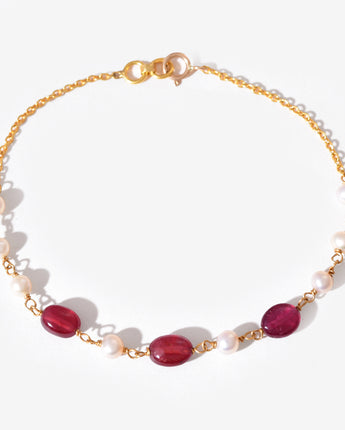 Gold bracelet with red gemstones and white pearls on a white background